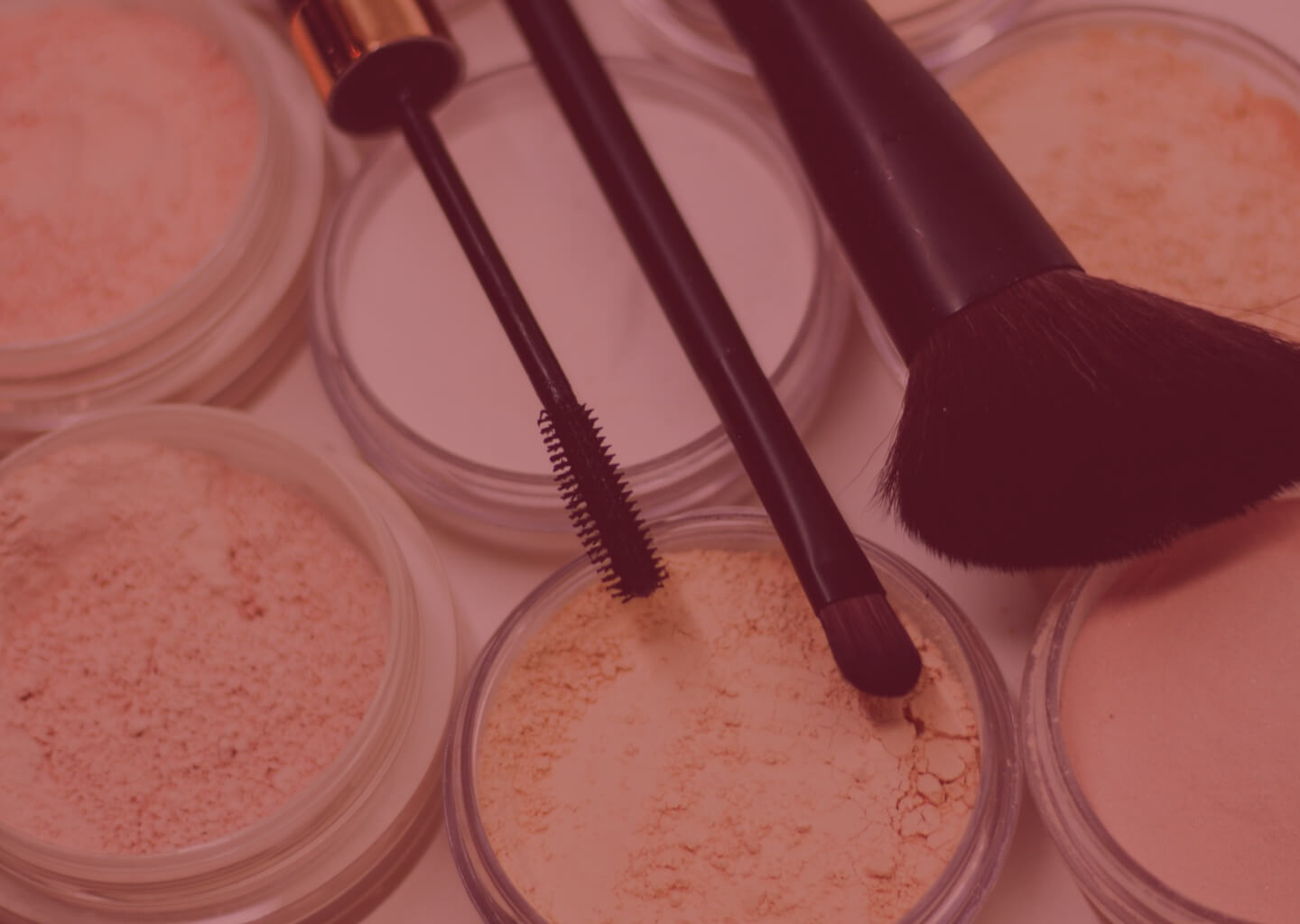 Several small containers of loose powder foundation with three black brushes sitting on top of them
